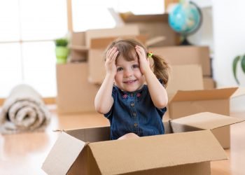 Child looking out of a box in new room after moving Child girl looking out of a box in new room after moving